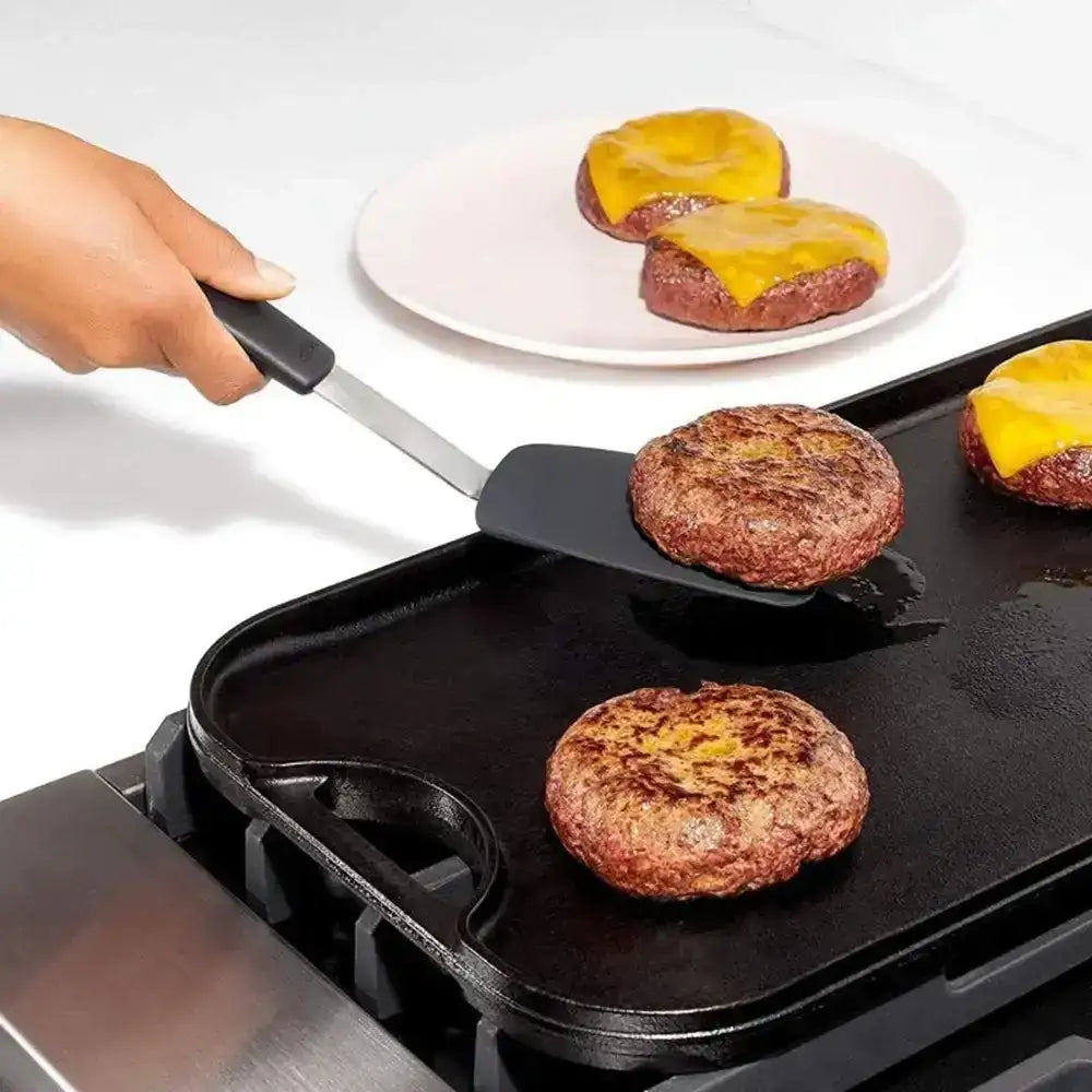 Person flipping burgers on a griddle with cheese using a spatula.