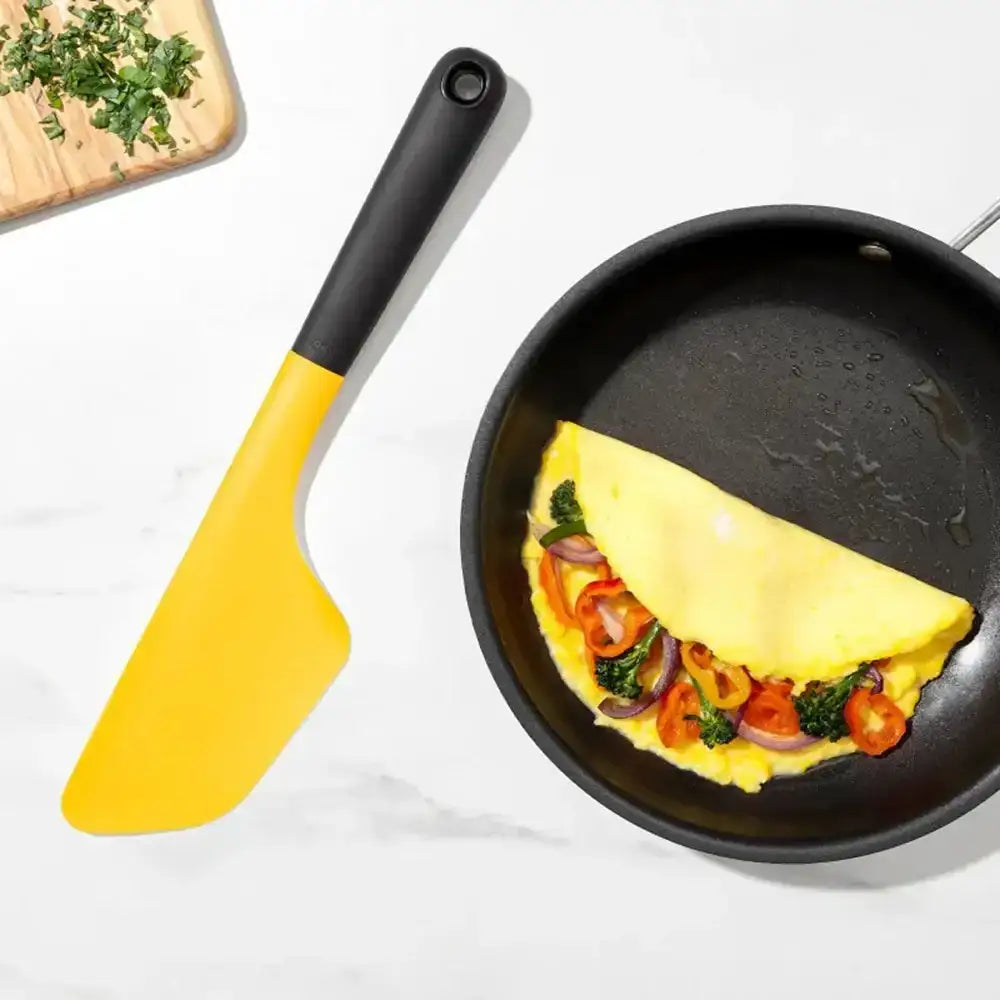 Omelette with vegetables in a frying pan with a yellow spatula on a white background