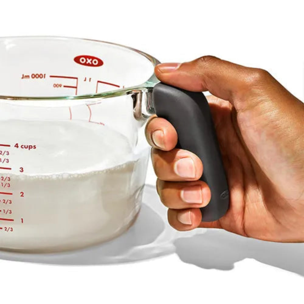 Hand holding an OXO measuring cup filled with liquid on a white background