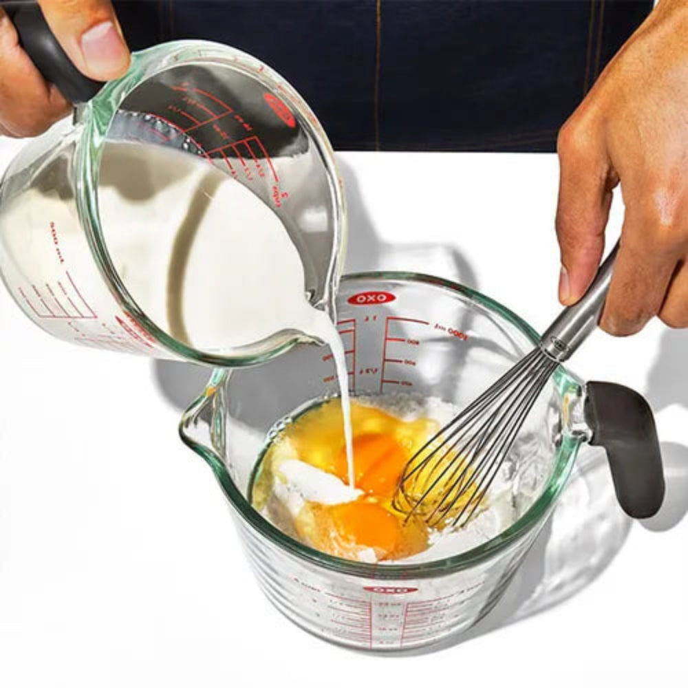 Person pouring milk into a measuring cup with eggs and a whisk.