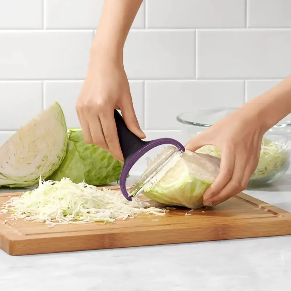 Person using a cabbage shredder on a cutting board with a white tiled wall background