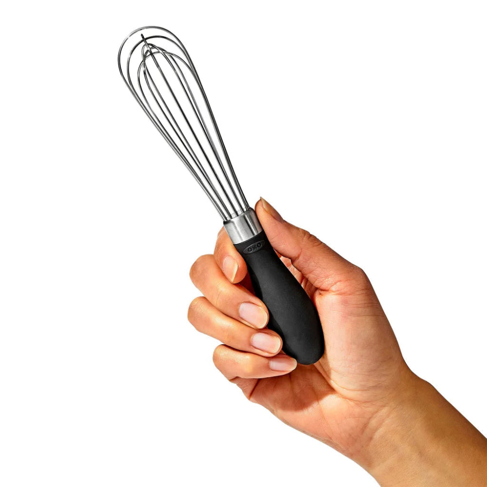 Hand holding a whisk with a black handle on a white background