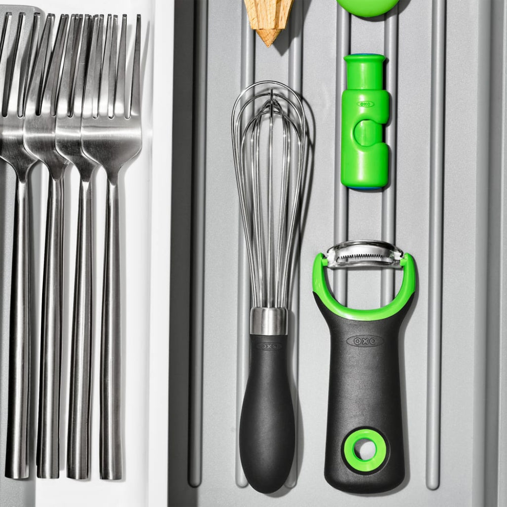 Set of kitchen utensils including forks, whisk, and peeler with green handles on a metallic surface.