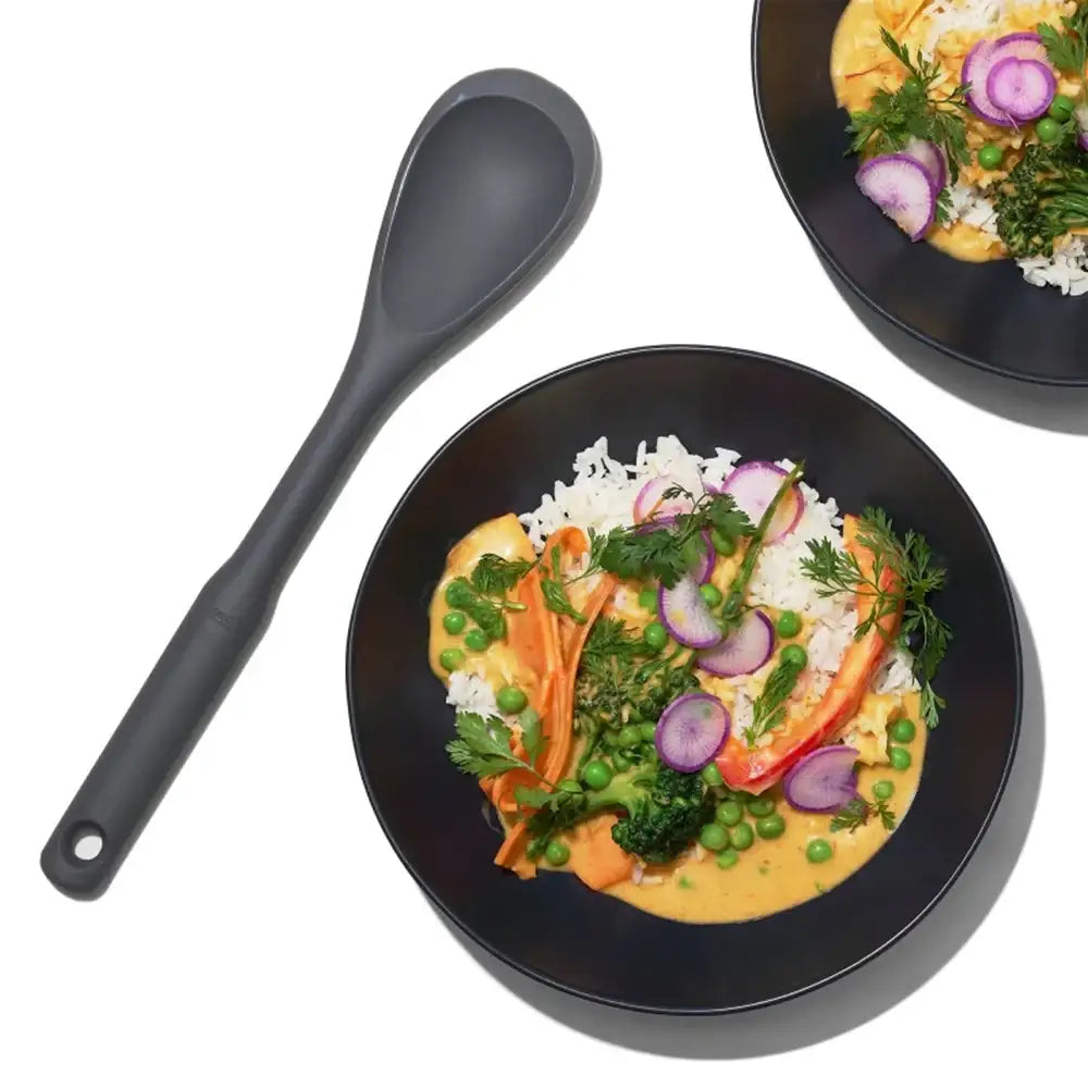 Black bowl with a colorful dish of rice, vegetables, and a spoon on a white background
