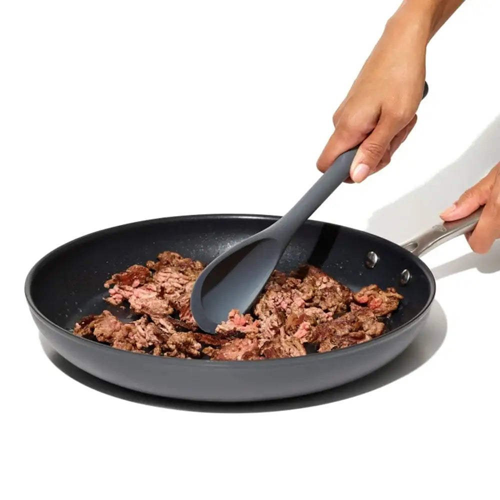 Person cooking meat in a frying pan with a spatula on a white background