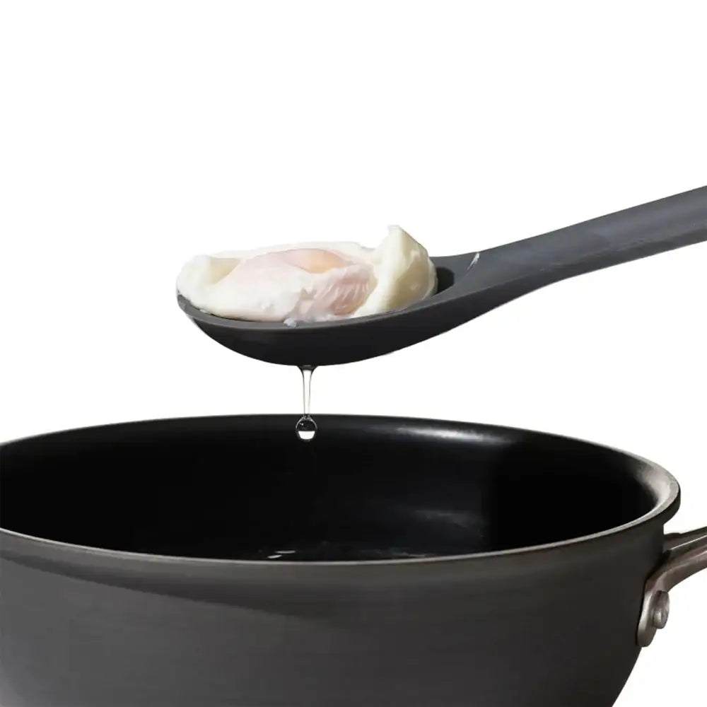 Egg being poured from a spoon into a black pot on a white background