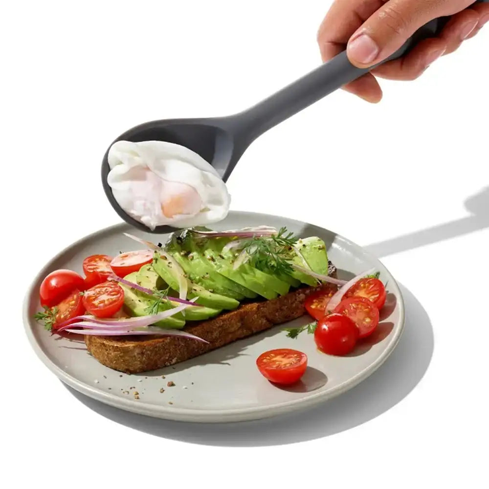 Spoon with a poached egg being added to a plate of avocado toast with tomatoes and onions.