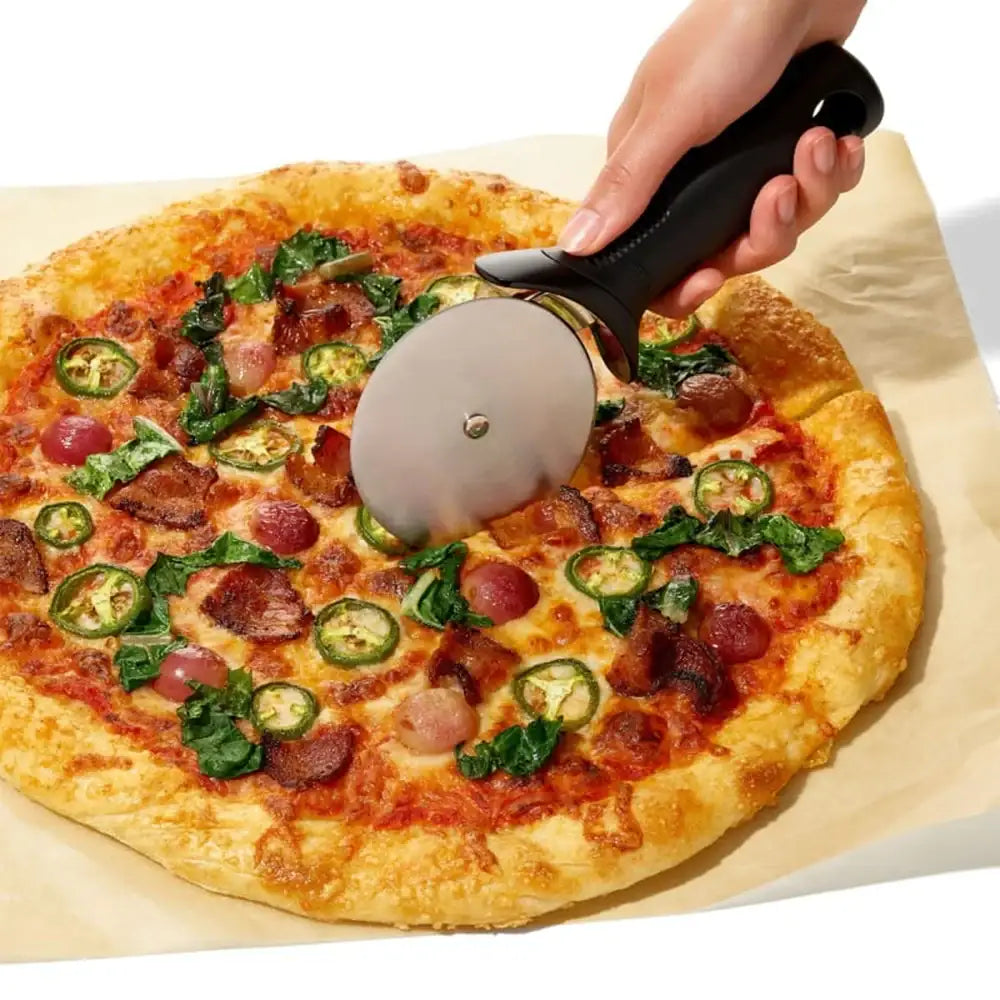 Person using a pizza cutter to slice a pizza with various toppings on a white background