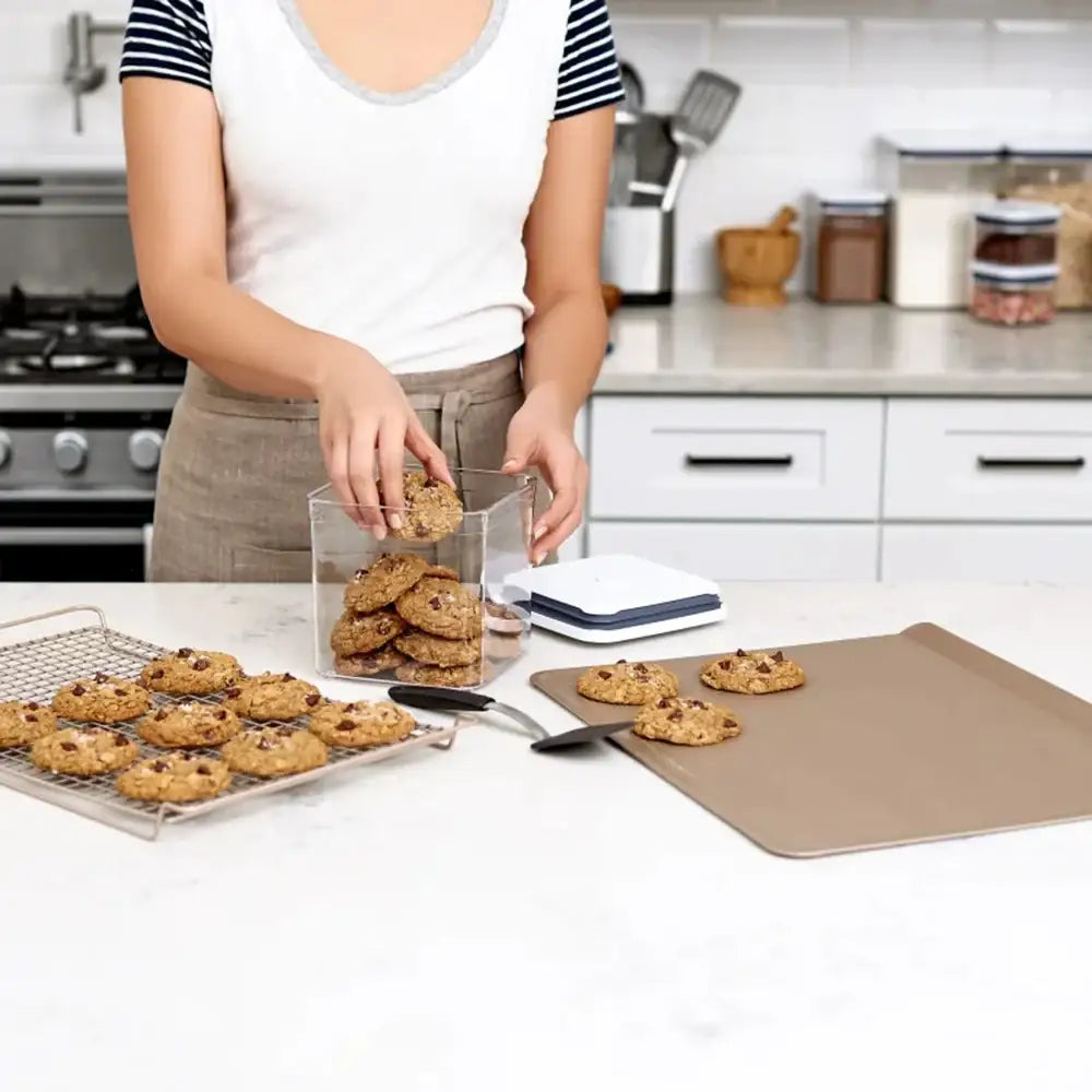 Person in a kitchen arranging cookies on a baking sheet and in a container.