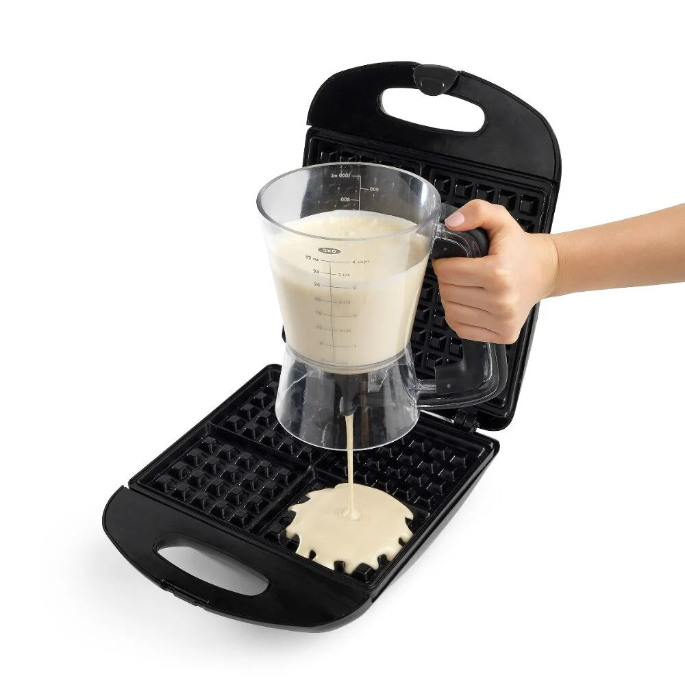 Person pouring batter into a black waffle maker on a white background