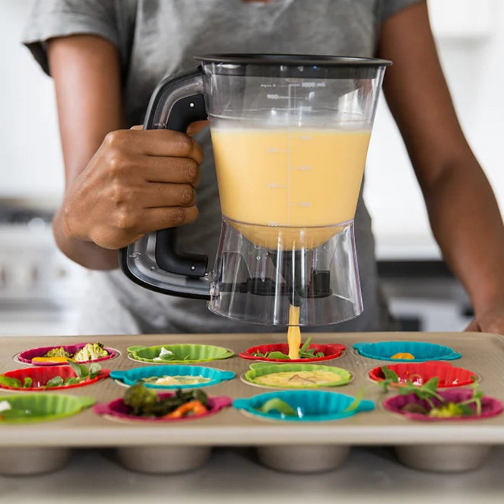 Person using a batter dispenser to pour liquid into colorful muffin molds.