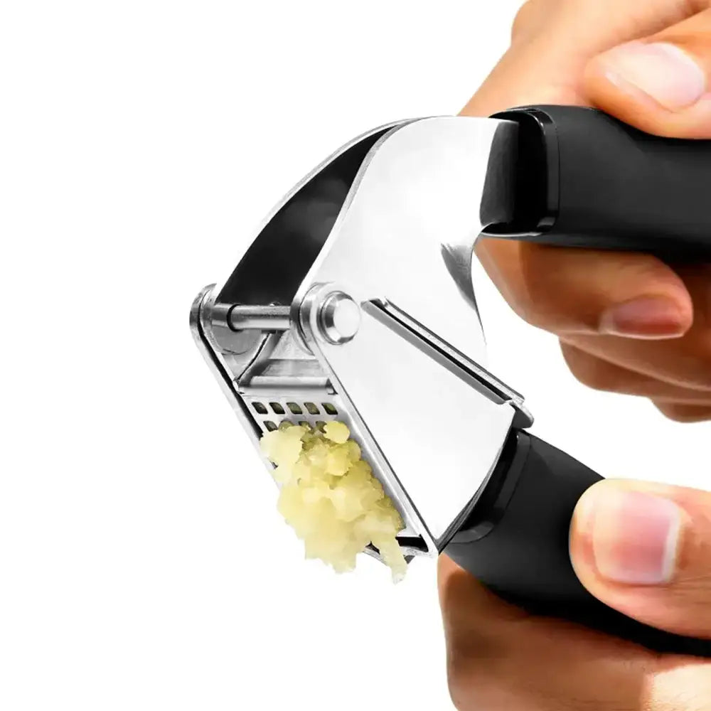Garlic press being used to crush garlic with a hand holding it on a white background