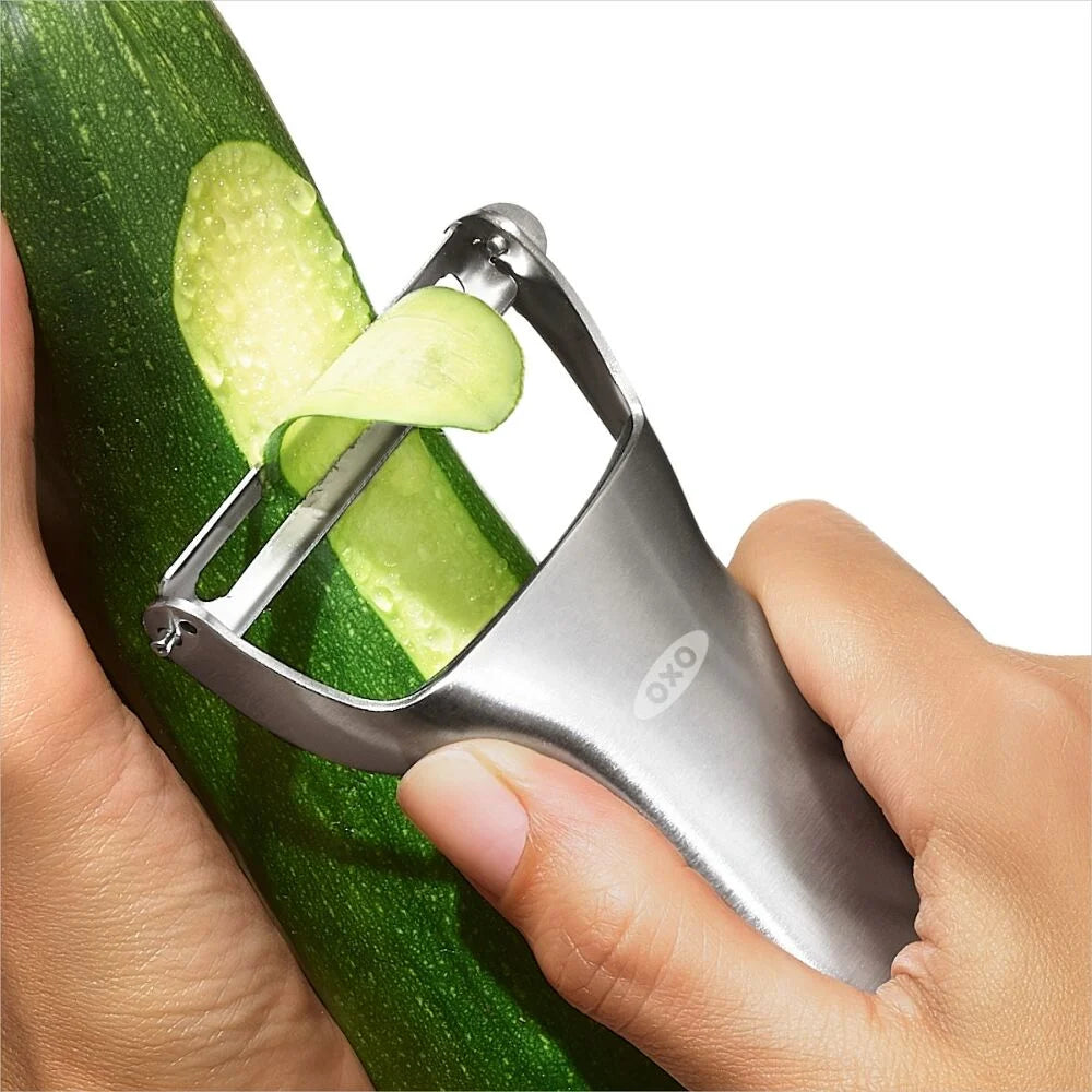 Oxo vegetable peeler being used to peel a zucchini on a white background