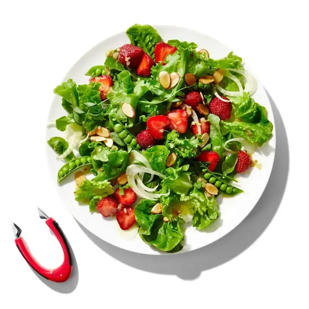 Salad with strawberries and nuts on a white plate with tongs.