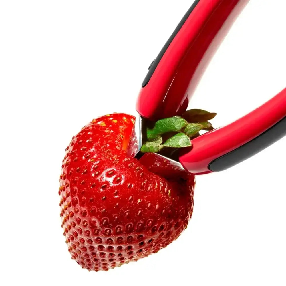 Red kitchen tool cutting a strawberry on a white background