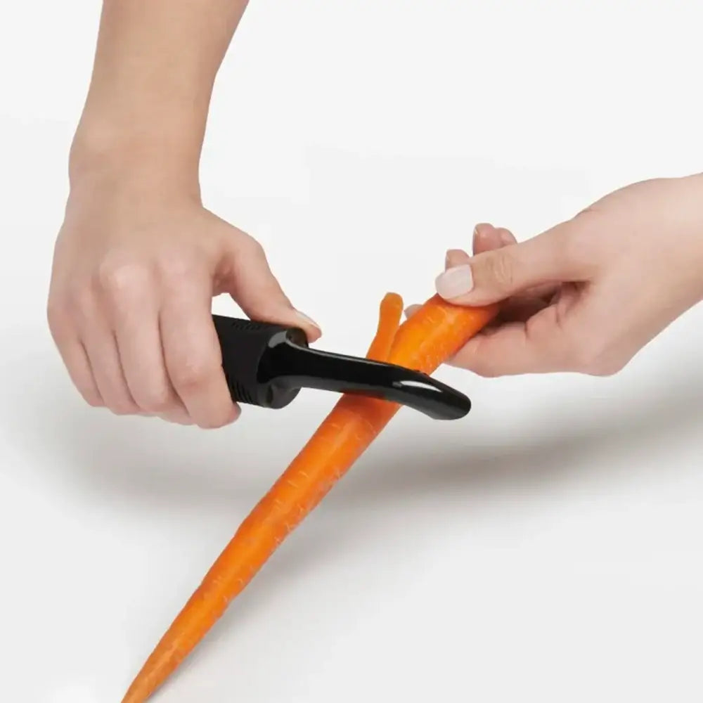 Person using a carrot peeler to peel a carrot on a white background