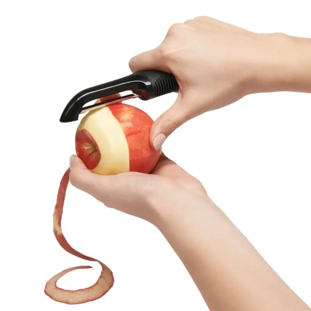 Person using a peeler to remove skin from an apple on a white background
