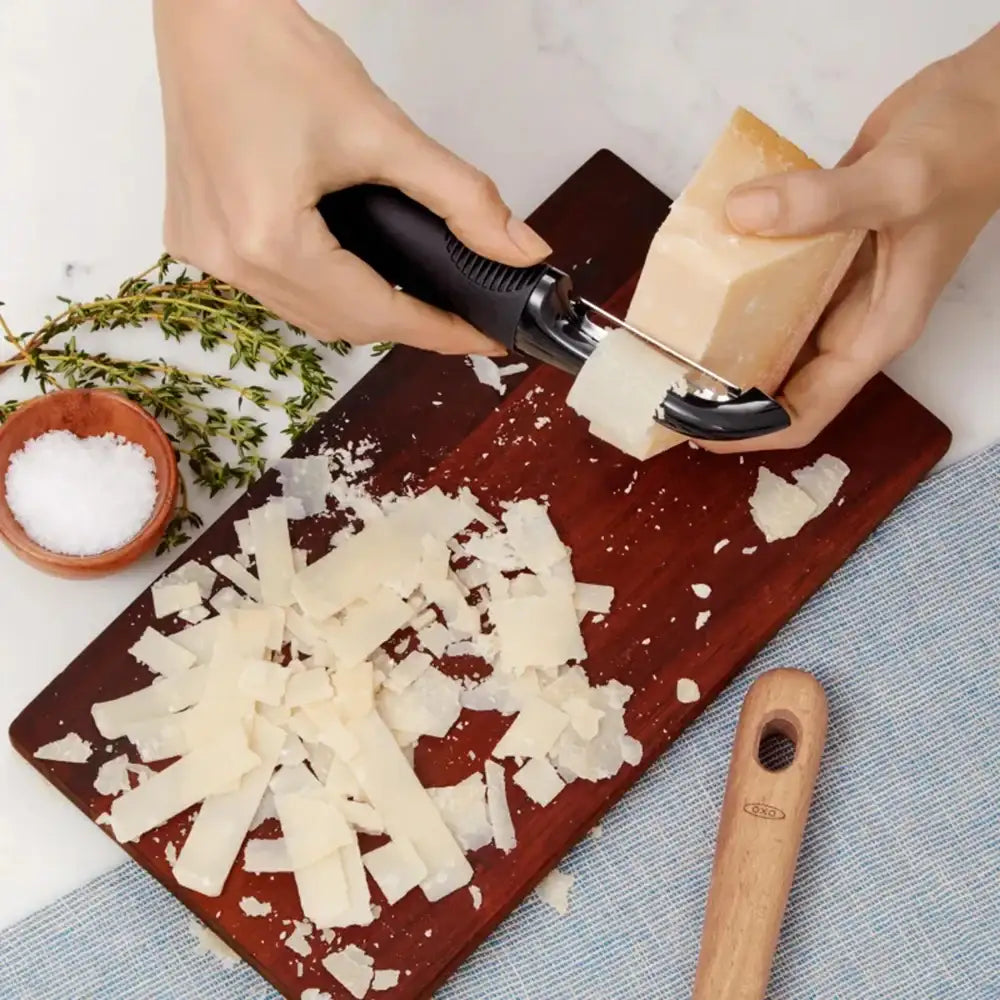 Person using a cheese grater on a block of cheese on a wooden cutting board with herbs and salt.