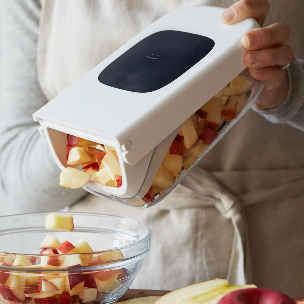 Person using a handheld fruit chopper to slice apples into a glass bowl.