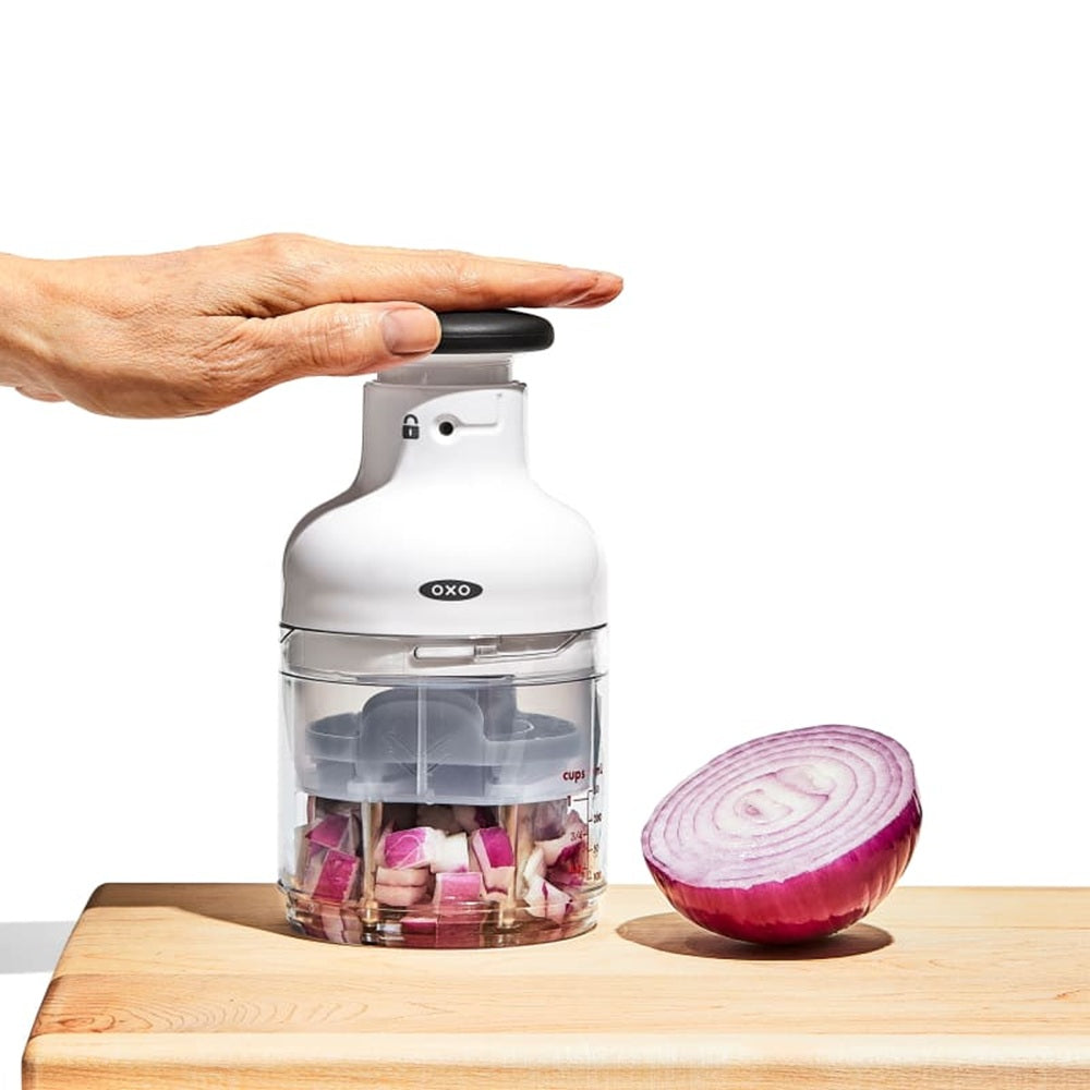 OXO hand chopper with chopped vegetables on a wooden cutting board