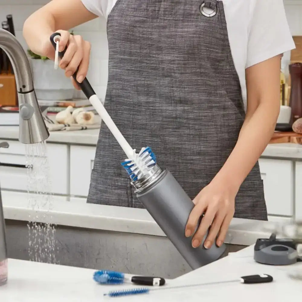 Person using a kitchen brush to clean a bottle in a kitchen setting