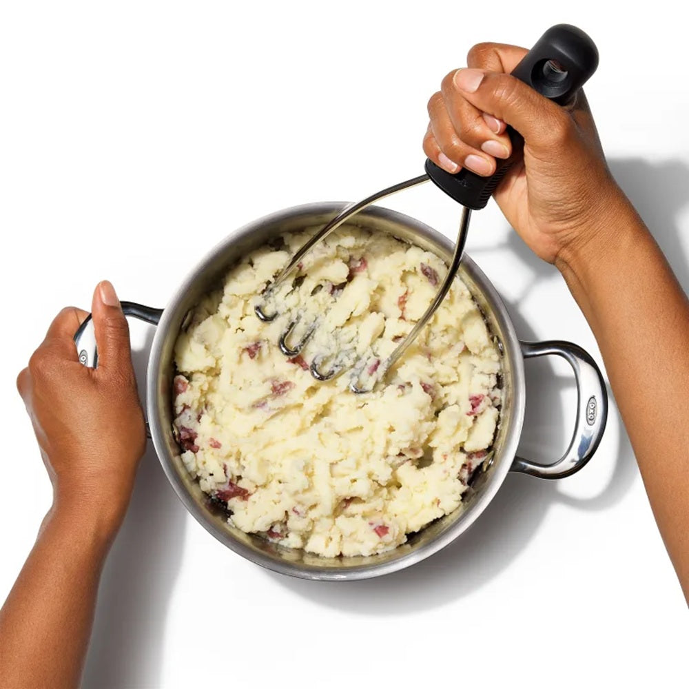 Person mashing potatoes in a pot with a masher on a white background