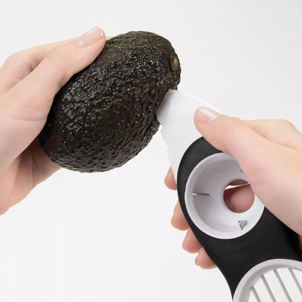 Hands using the avocado slicer to cut open an avocado