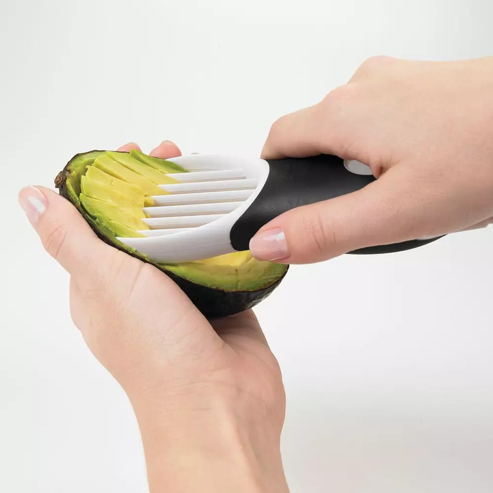A hand using the oxo avocado slicer to slice through an avocado