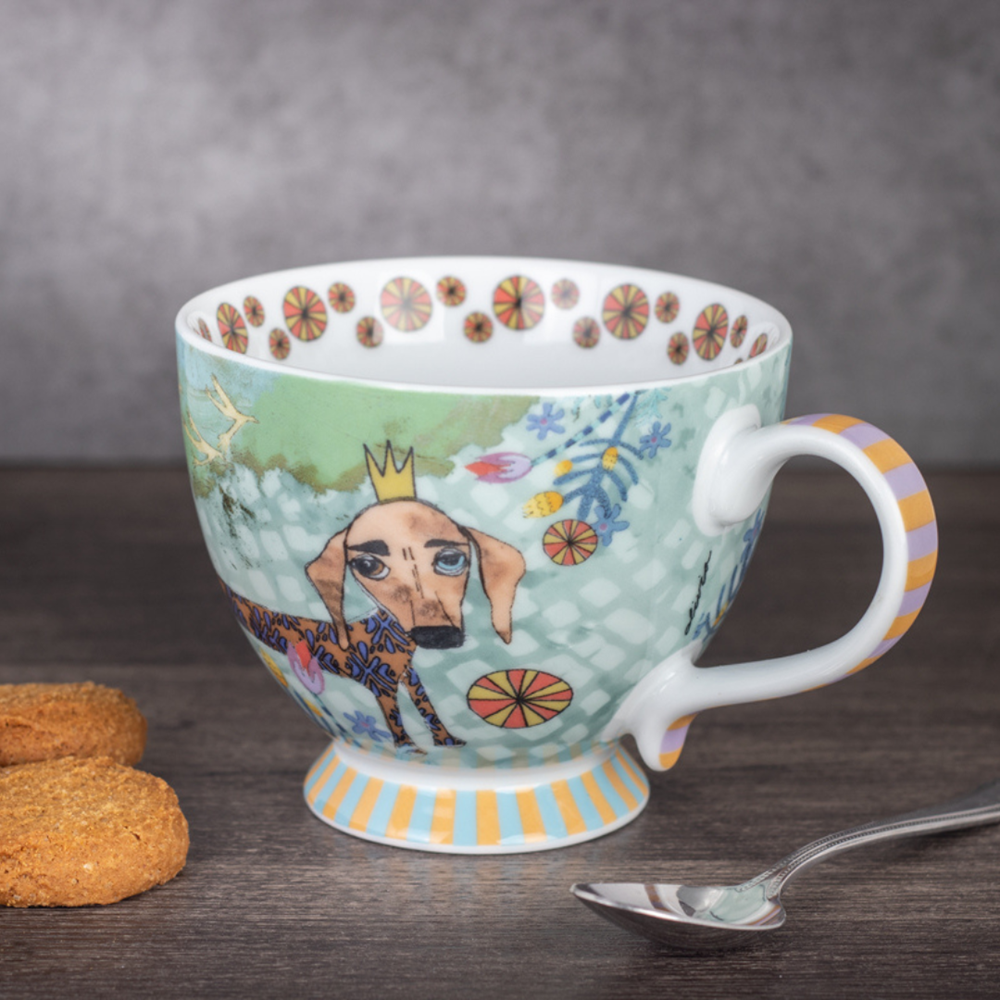 Decorative mug with a dog illustration on a wooden surface with cookies and a spoon.