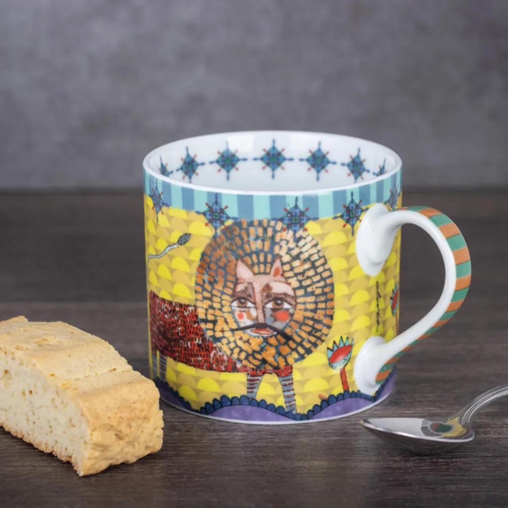 Colorful mug with artistic design on a wooden surface with a cookie and spoon.