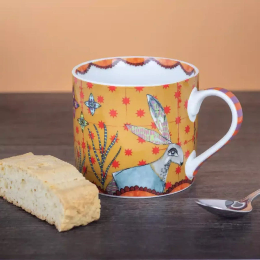Colorful mug with floral design, biscuit, and spoon on a wooden surface