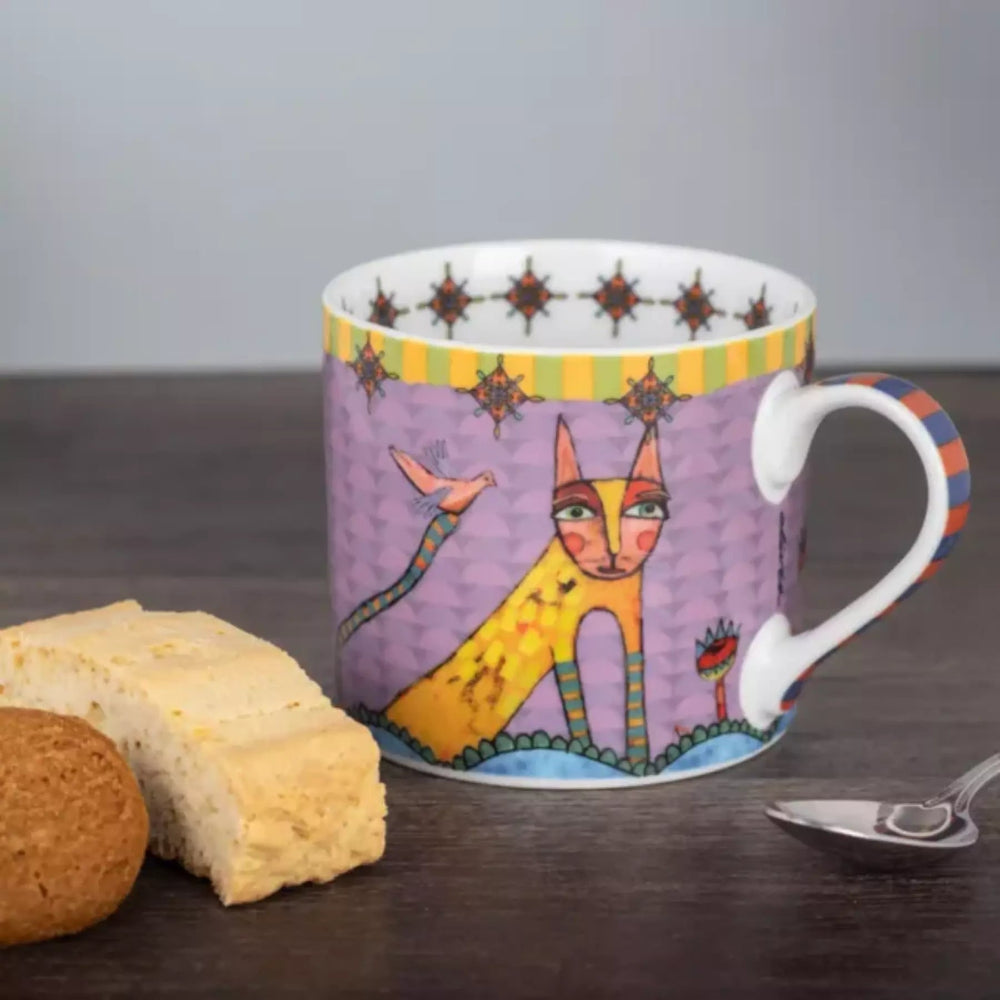 Colorful mug with artistic design on a wooden surface with cookies and a spoon.
