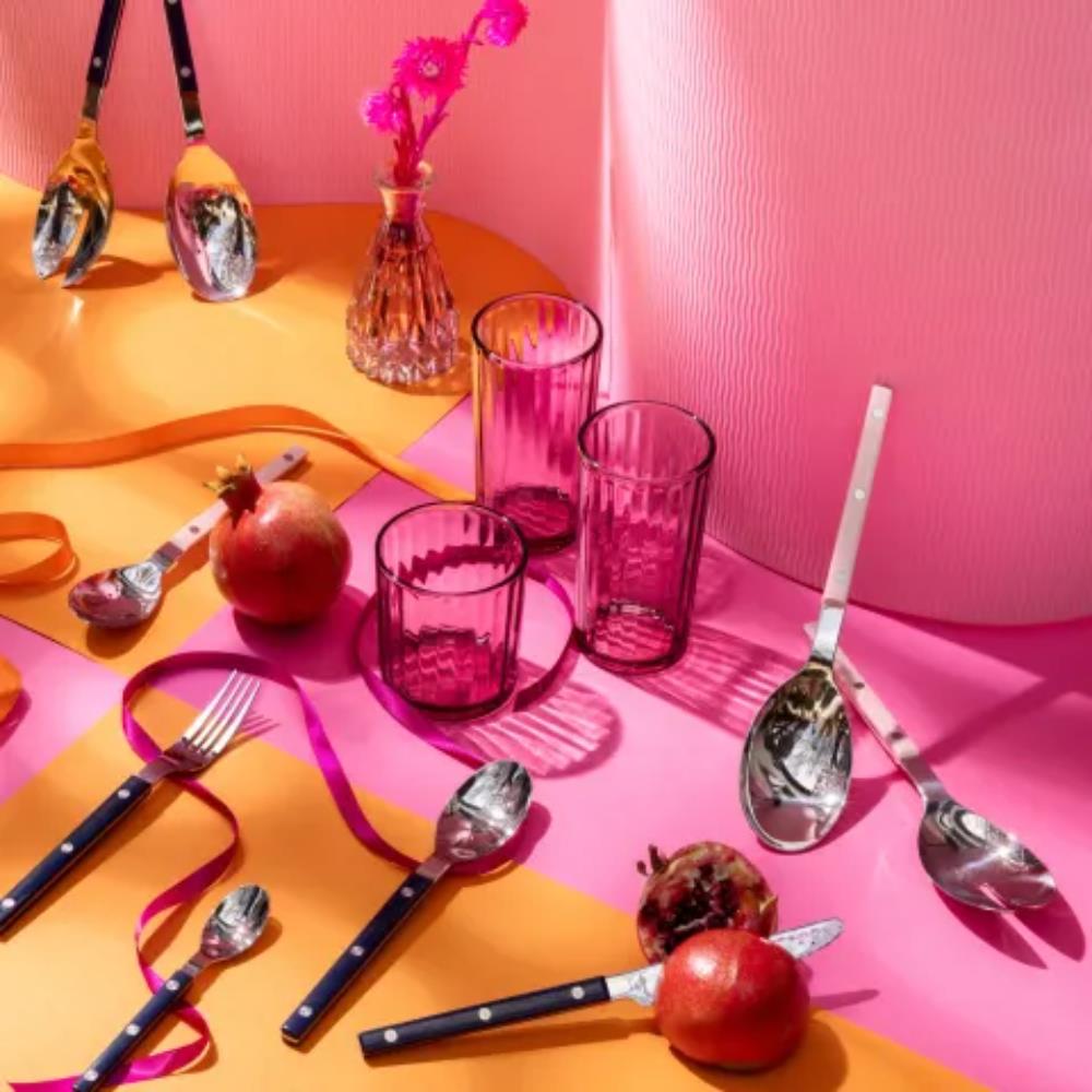 Colorful table setting with glasses, apples, and utensils on a pink and orange background