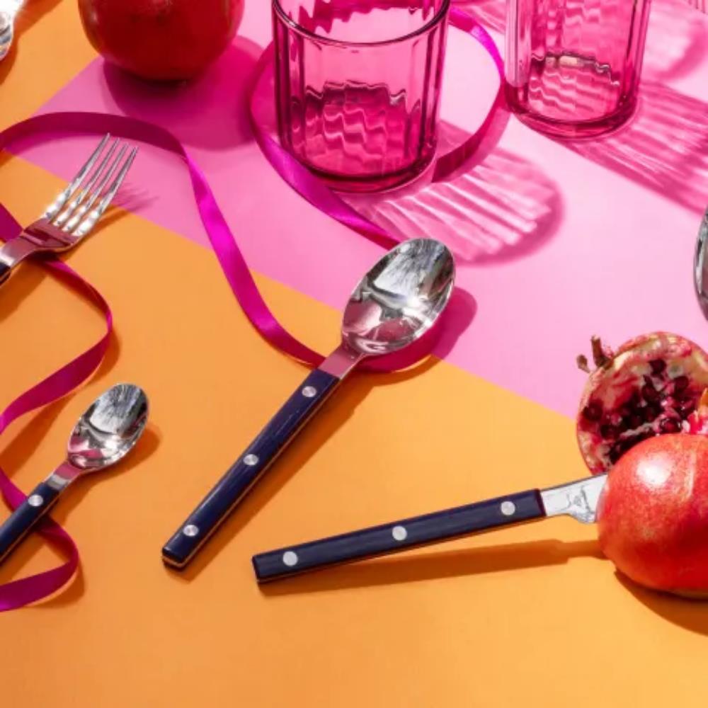 Table setting with cutlery, glasses, and pomegranates on a colorful background