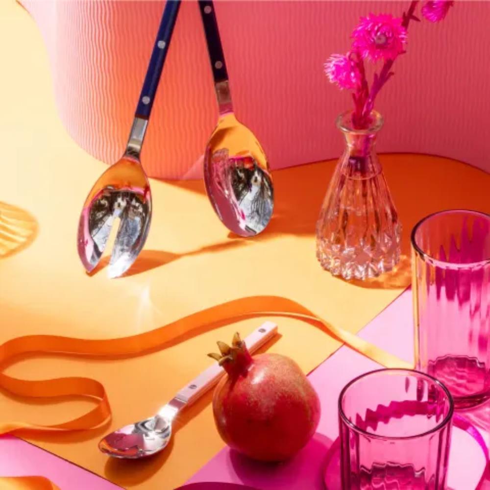 Colorful still life with spoons, a pomegranate, and a vase on a pink and orange background.