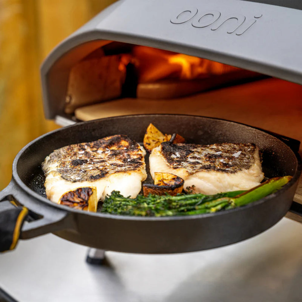 Person placing a skillet into an Ooni pizza oven 