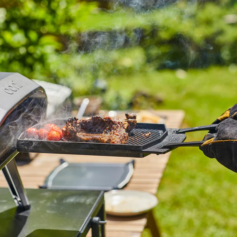 Person grilling meat and vegetables on a portable grill outdoors.