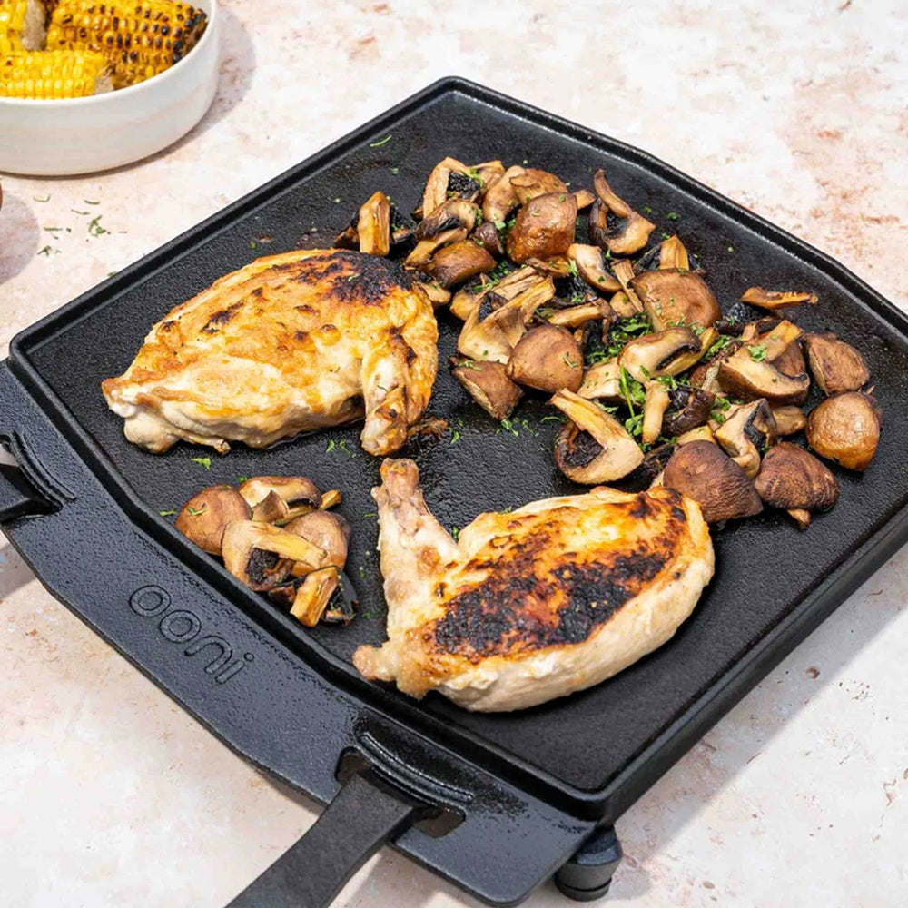 Grilled chicken and mushrooms on a cast iron skillet with 'Ooni' branding.