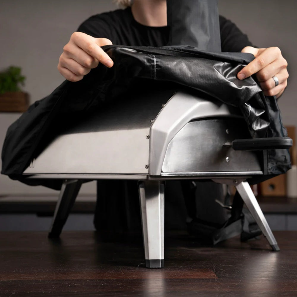 Person opening a black cover on a small outdoor pizza oven.