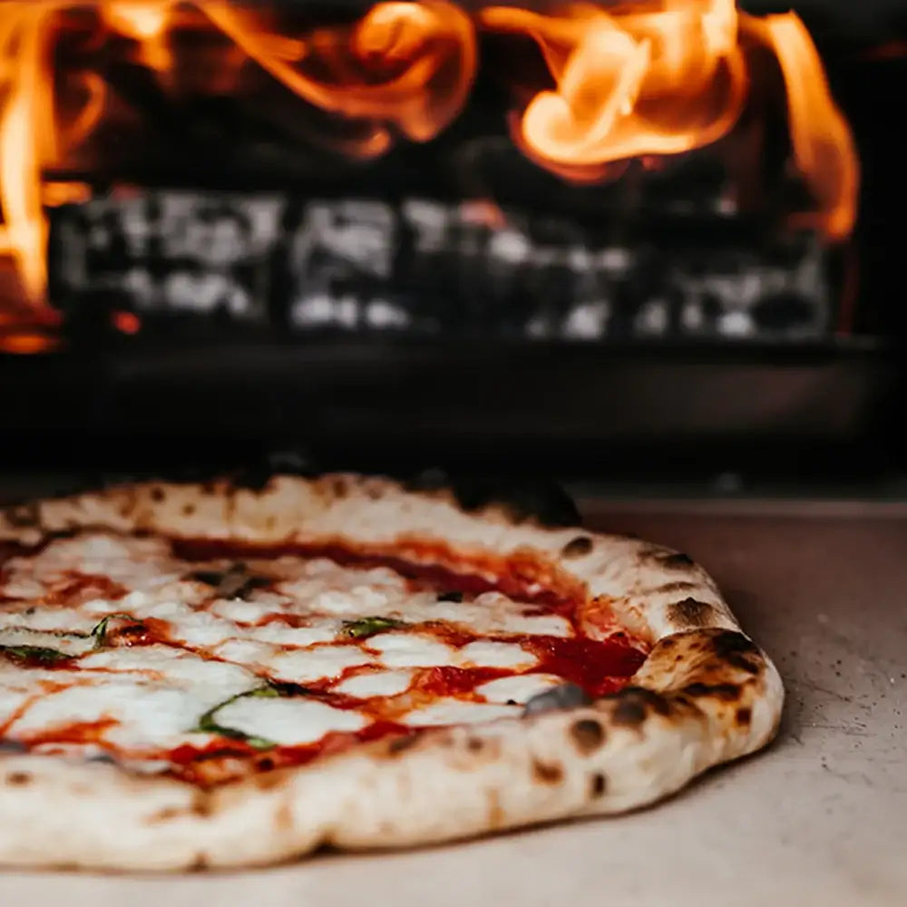 Margherita pizza being cooked in a wood-fired oven with flames.