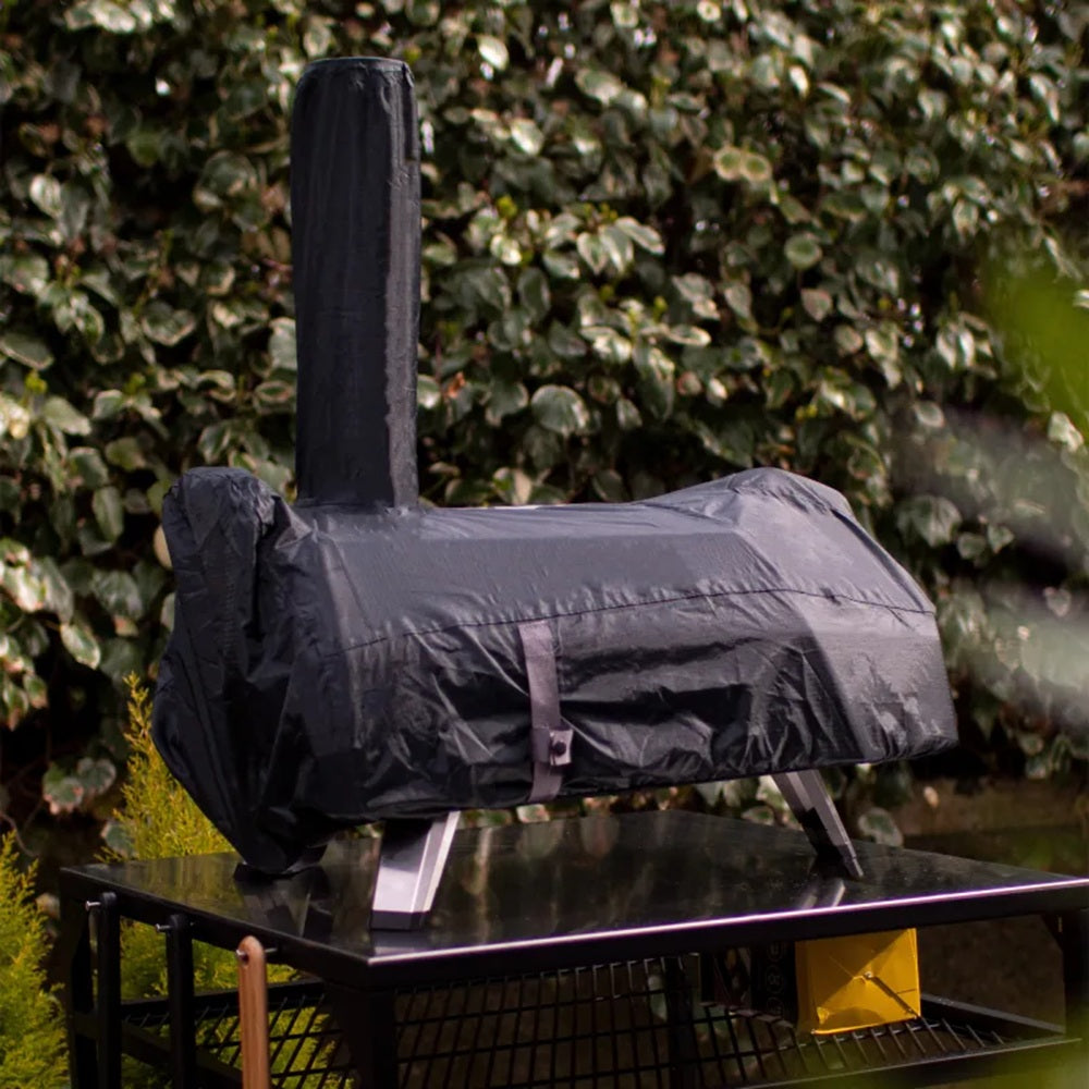 Black grill cover on a grill with green foliage in the background