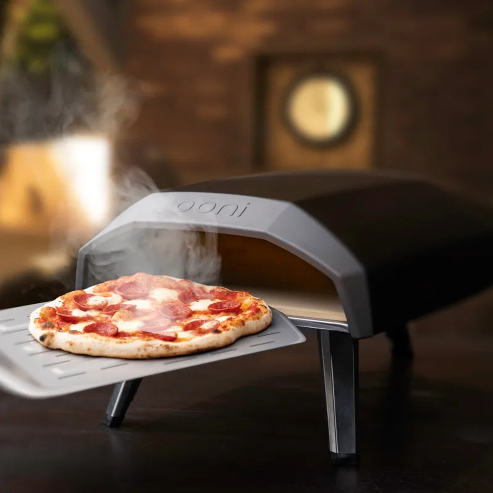Portable pizza oven with a pizza inside, set against a warm-toned background.