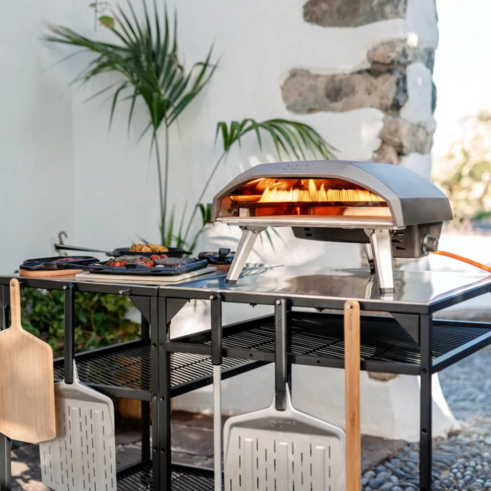 Outdoor pizza oven on a stand with a stone wall and plants in the background