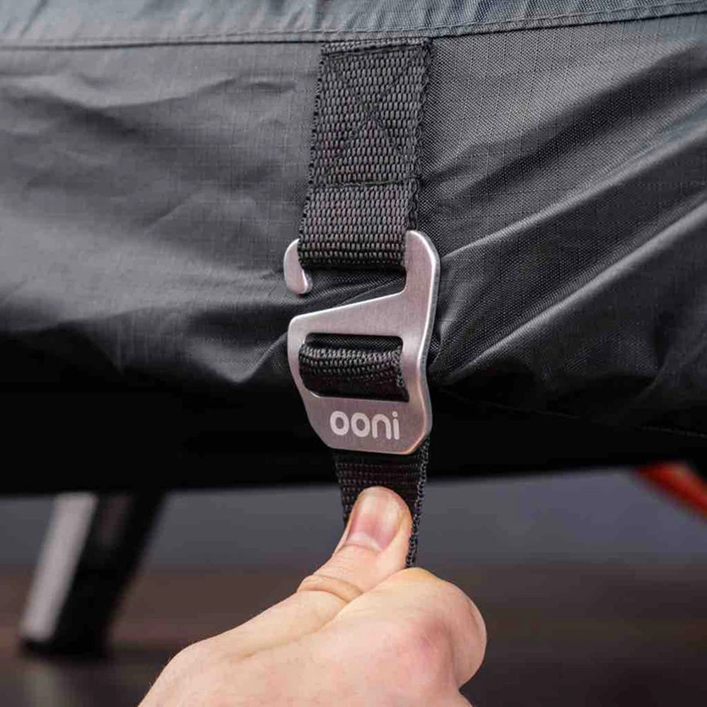 Close-up of a person adjusting a strap on a black bag with 'ooni' branding.