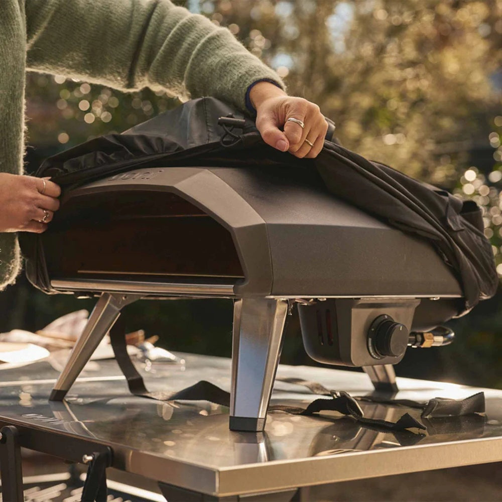 Person opening a portable outdoor oven on a table with a blurred natural background