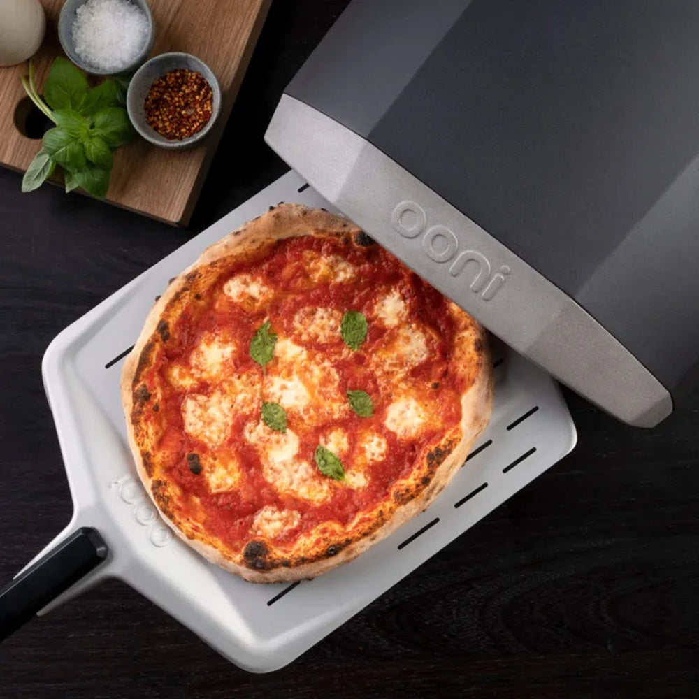 Pizza on a portable pizza oven with 'Onni' branding on a dark surface.