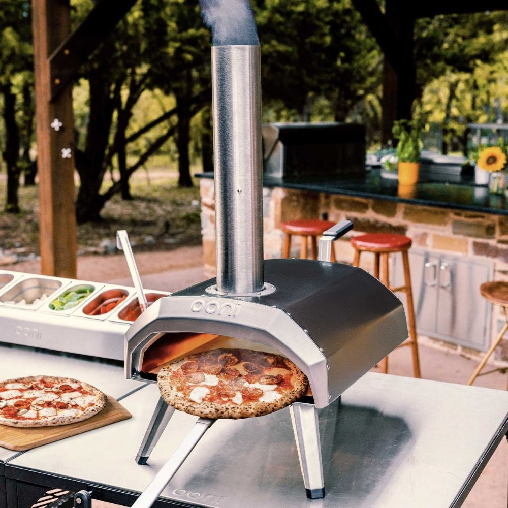 Outdoor pizza oven with a pizza being cooked, set up in a backyard with outdoor furniture.