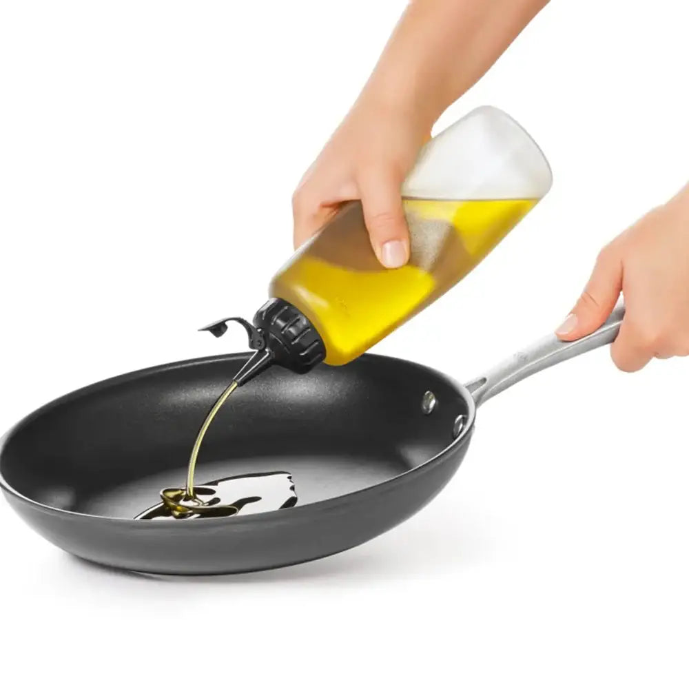 Person pouring oil from a bottle into a frying pan on a white background