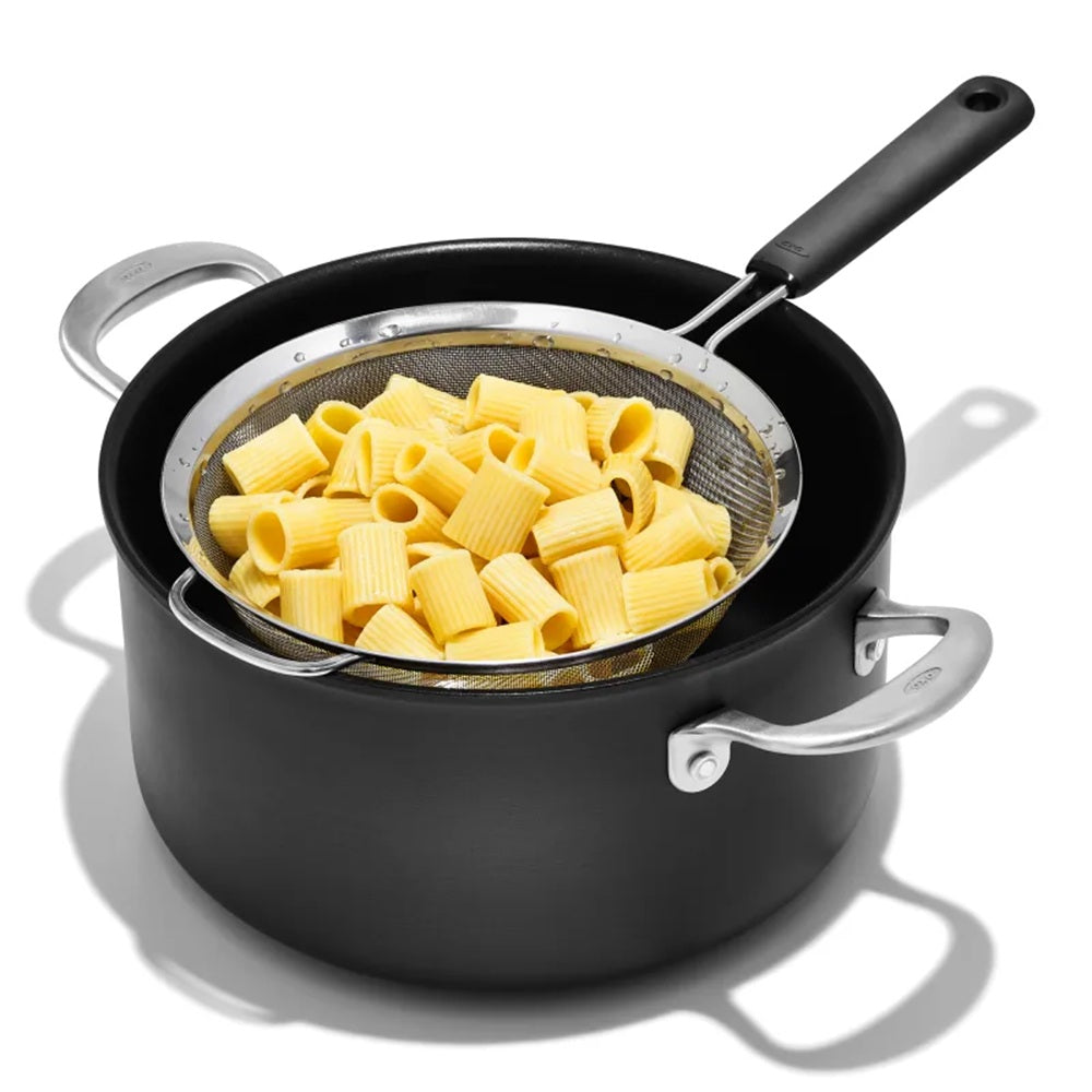 Black pot with a strainer containing cooked pasta on a white background