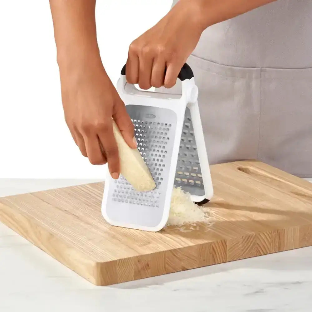 Person using a white grater on a wooden cutting board with a white background
